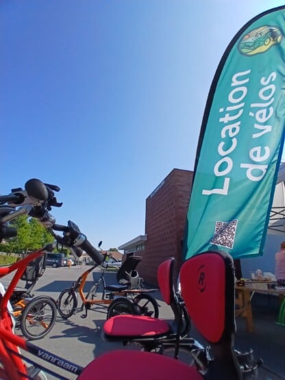 Vélos disponibles à la location, incluant modèles adaptés et vélos électriques, sous un ciel bleu.