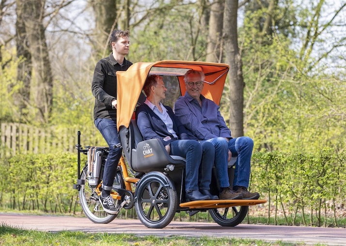 Vélo adapté avec canopy pour trois passagers, roulant dans un parc verdoyant.