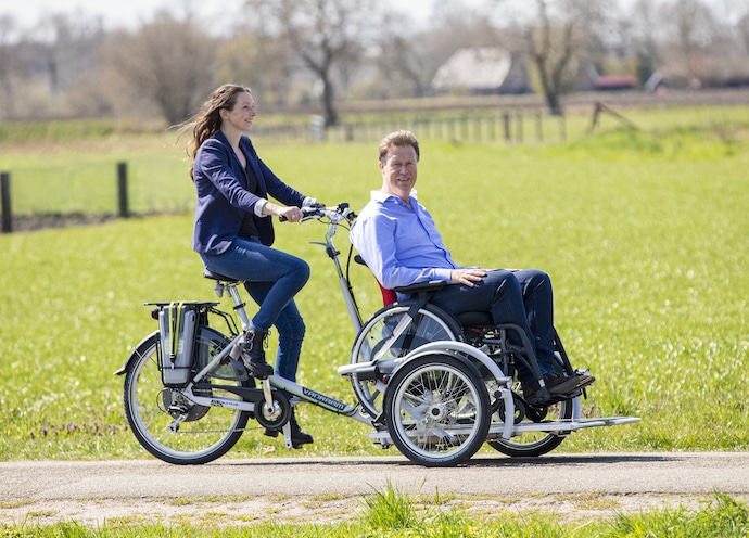 Femme pédalant sur un vélo tandem adapté pour personne à mobilité réduite dans un paysage verdoyant.