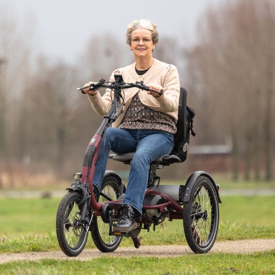 Femme souriante sur un tricycle adapté, roulant sur un chemin en pleine nature.