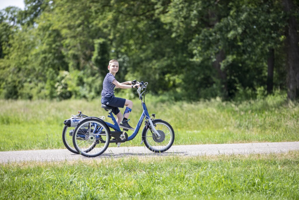 Enfant sur un vélo adapté à trois roues, profitant d'une promenade en pleine nature.