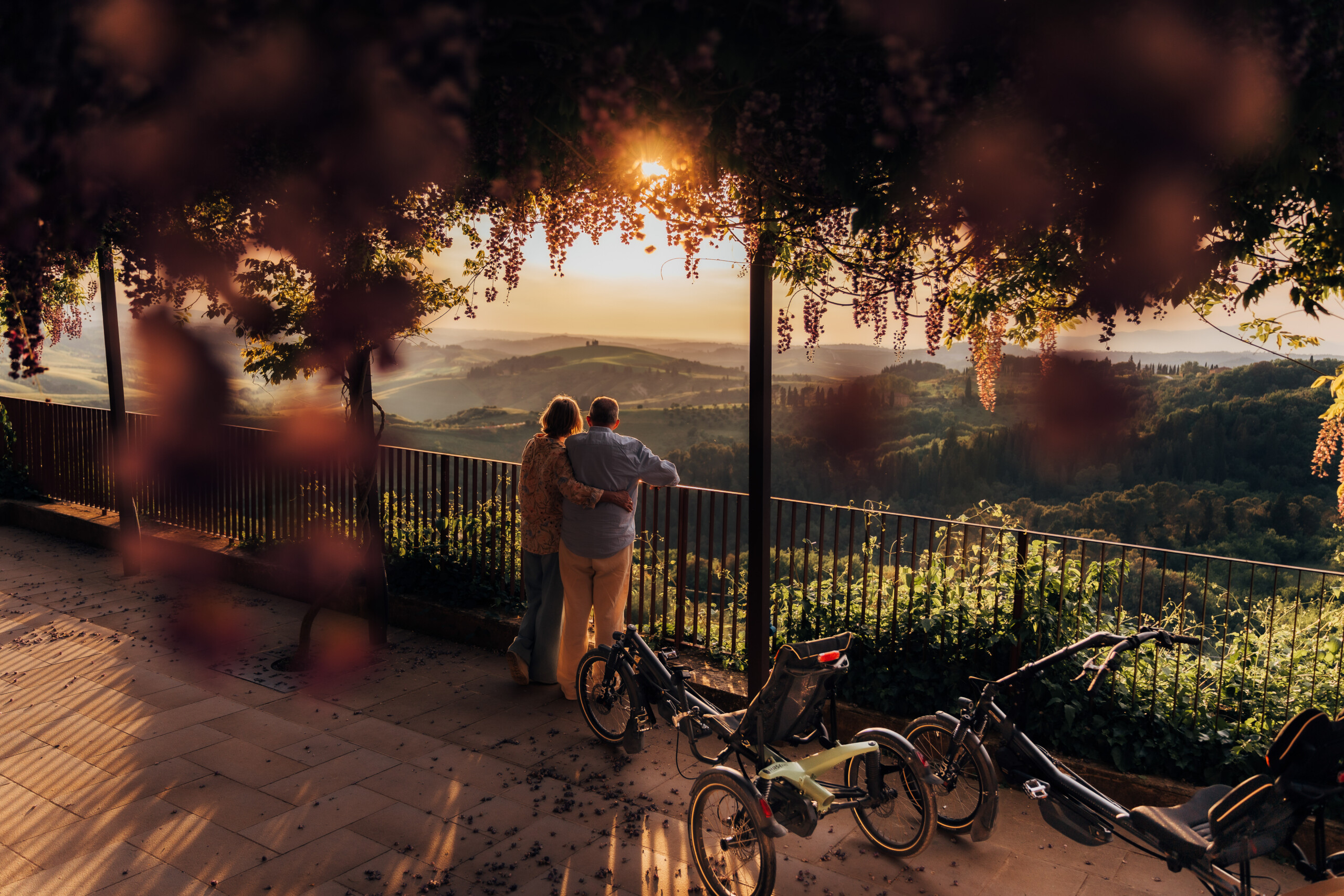 Un couple admire le paysage avec des vélos stationnés à côté d'eux, entourés de fleurs au coucher de soleil.