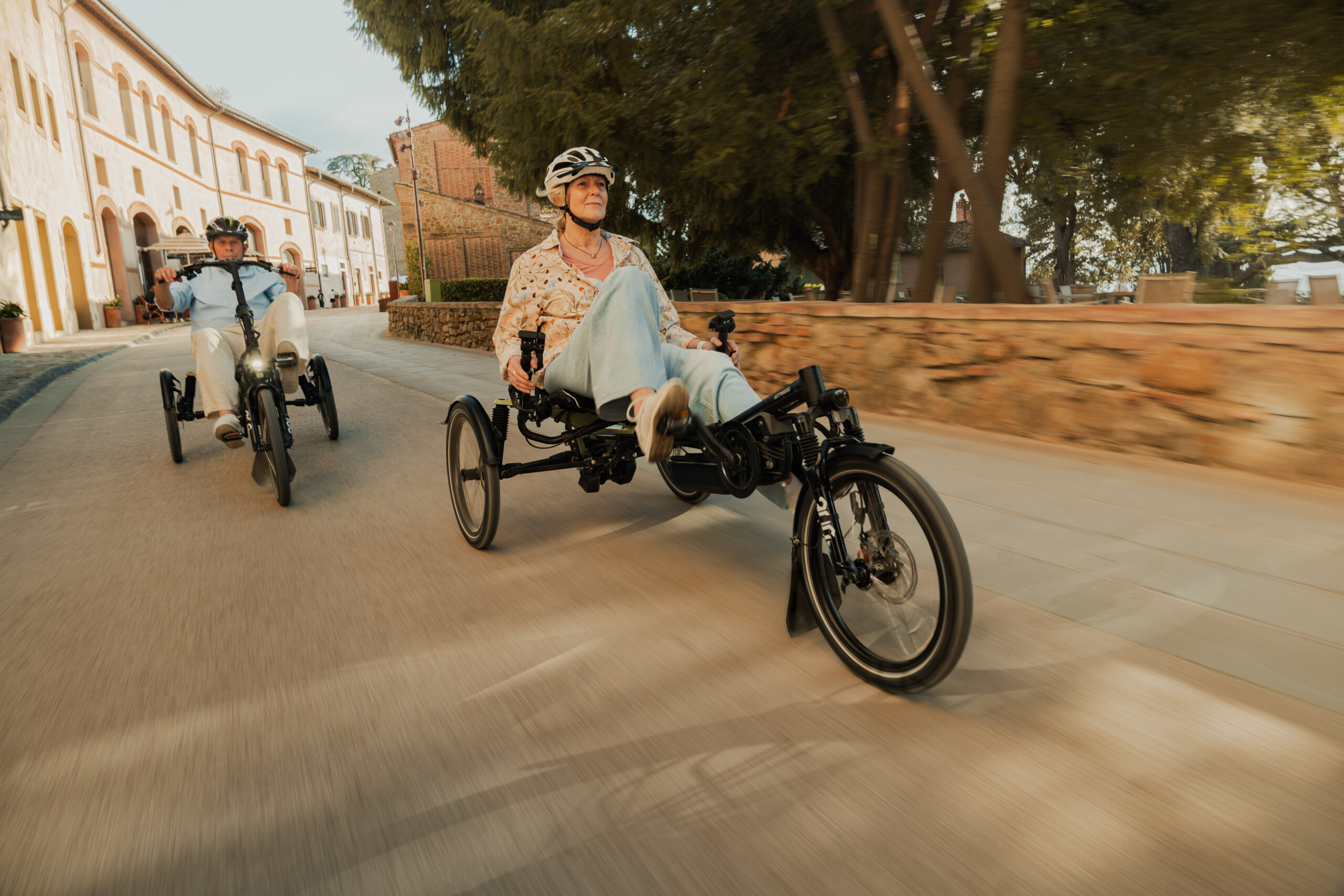 Deux personnes circulent sur des vélos adaptés dans une rue, entourées d'un paysage architectural.