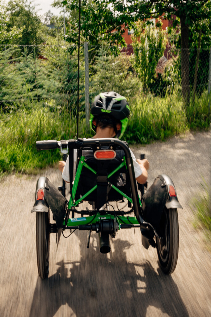 Enfant pédalant sur un vélo adapté, chemin de gravier entouré de verdure.