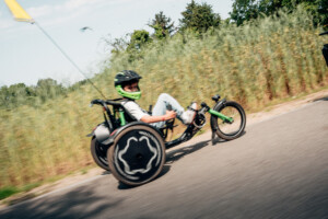 Enfant sur un vélo adapté, se déplaçant sur une route, entouré de végétation.