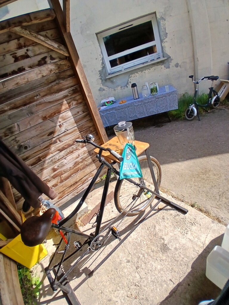 Vélo noir stationné sous un abri, avec une table en arrière-plan, représentant l'offre de Roulez JEUnesse Loisirs.