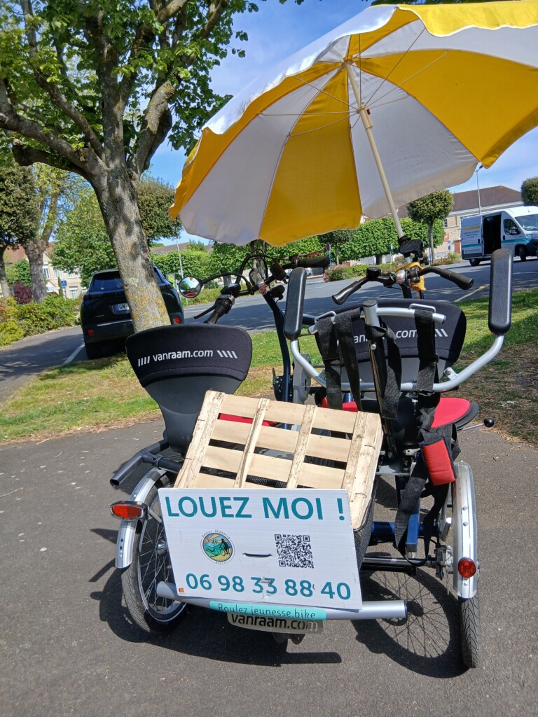 Vélo adapté Van Raam avec parasol et panneau de location dans un parc.