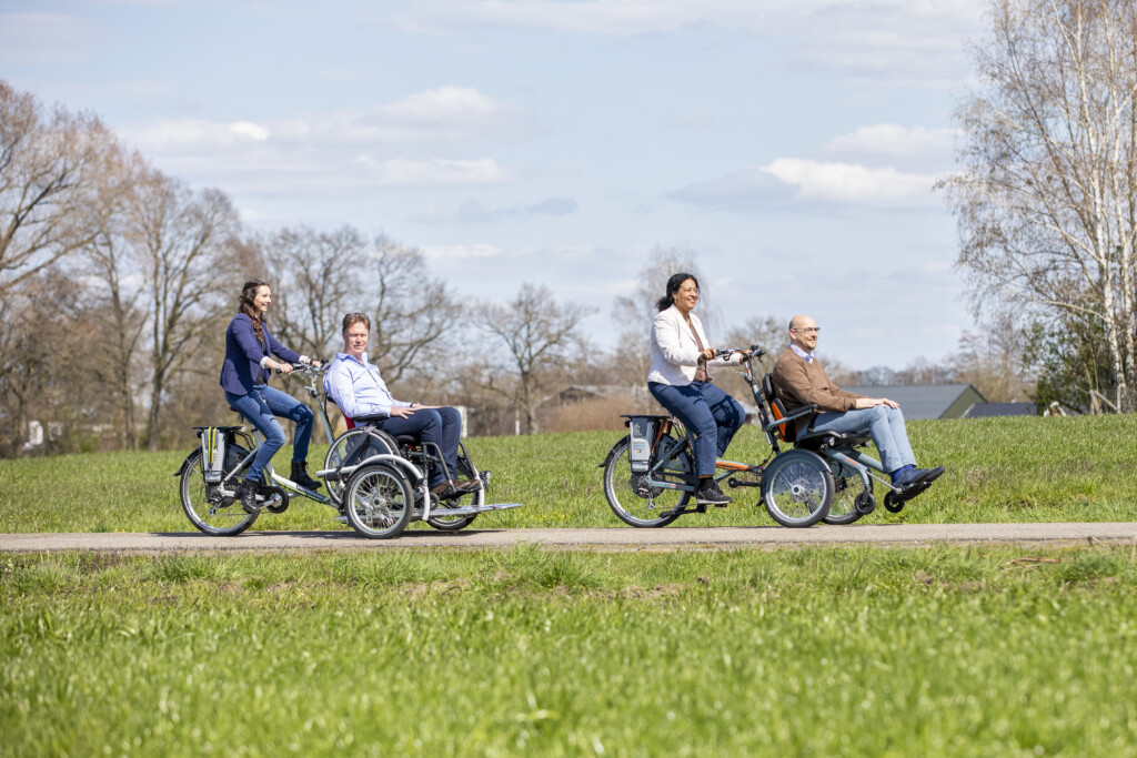 Quatre personnes se promenant à vélo, dont deux sur des vélos adaptés à mobilité réduite, dans un cadre paisible.