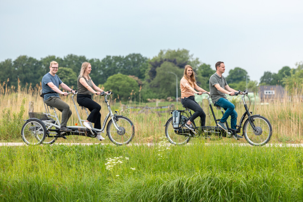 Quatre personnes pédalant sur des vélos, dont un tandem, dans un paysage verdoyant.