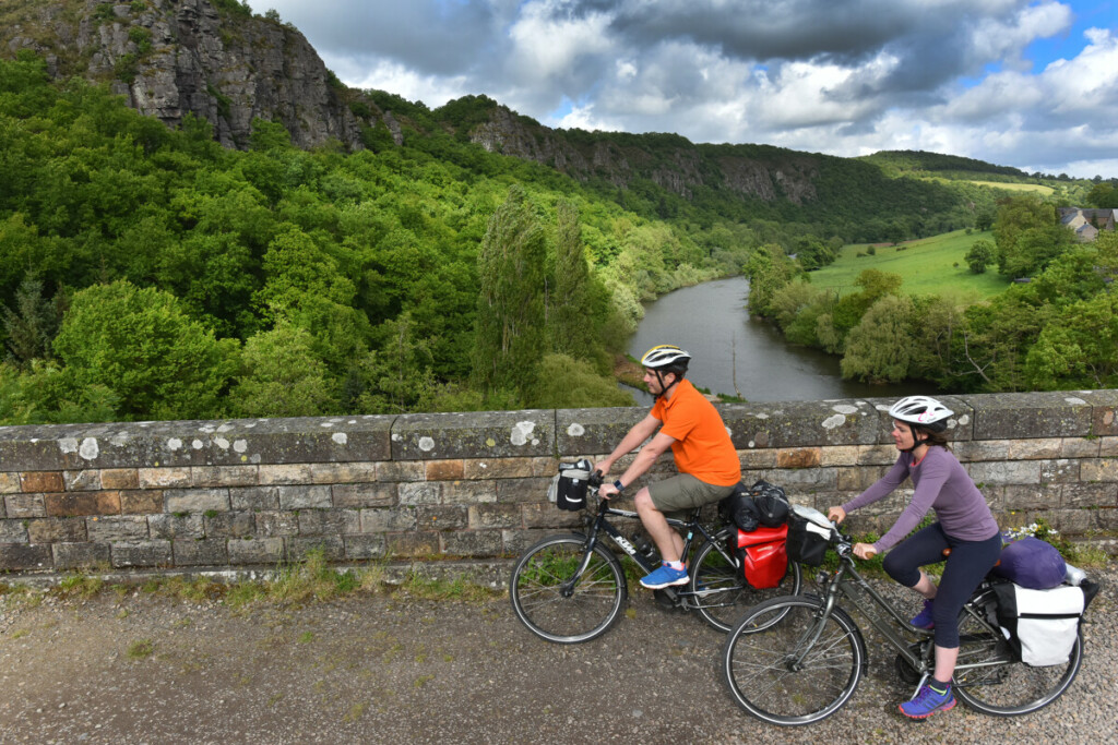 Deux cyclistes avec des bagages profitent d'un paysage verdoyant près d'une rivière, lors d'une balade à vélo.