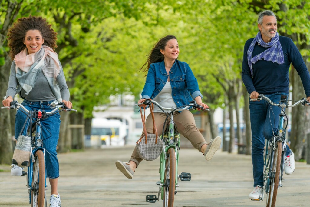 Trois cyclistes souriants sur des vélos, entourés de verdure dans un parc.