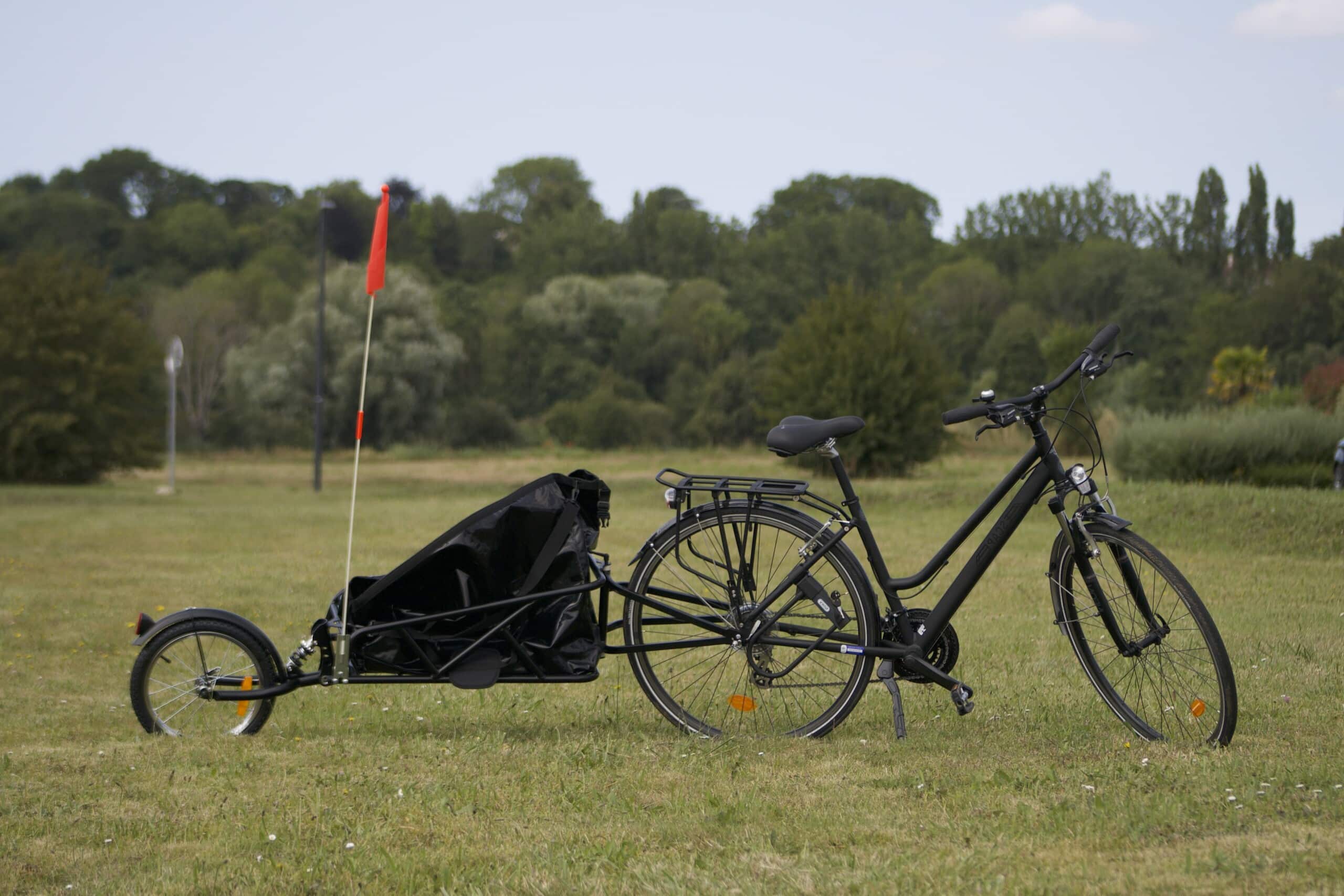 Vélo de ville avec remorque noire sur terrain verdoyant, adapté pour le transport d'enfants ou de charges légères.